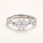 Silver-colored four leaf clover ring on a white background, with four clear heart-shaped stones, crossing band lines, bead accents, and an overlapping open back.