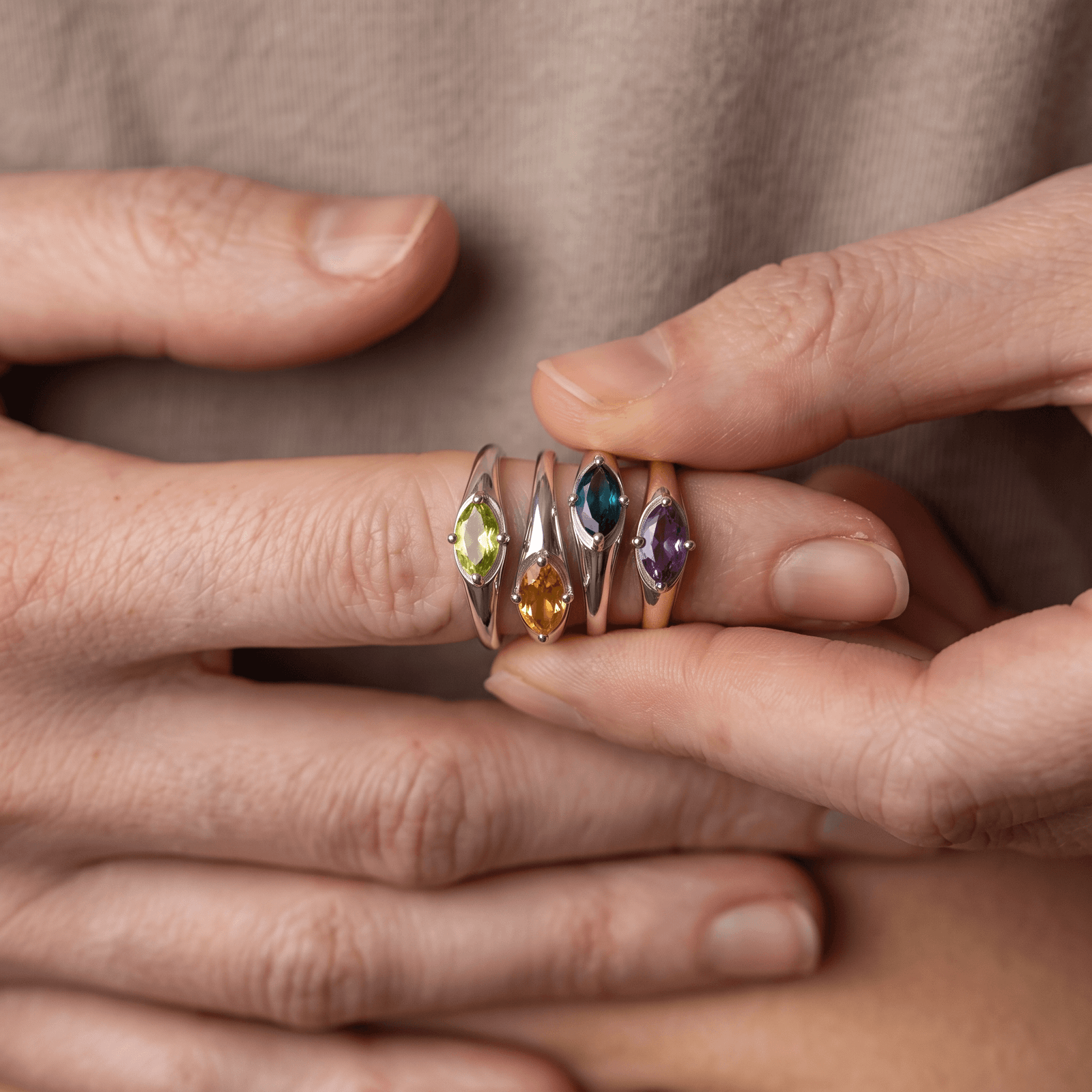 Four silver-colored marquise gemstone rings held together on a finger, with the yellow-green peridot ring at the left.