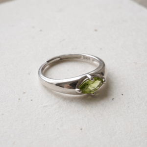 Front view of a marquise peridot ring on a white background, showing the horizontal yellow-green gemstone, four-prong setting, and overlapping silver-colored band.