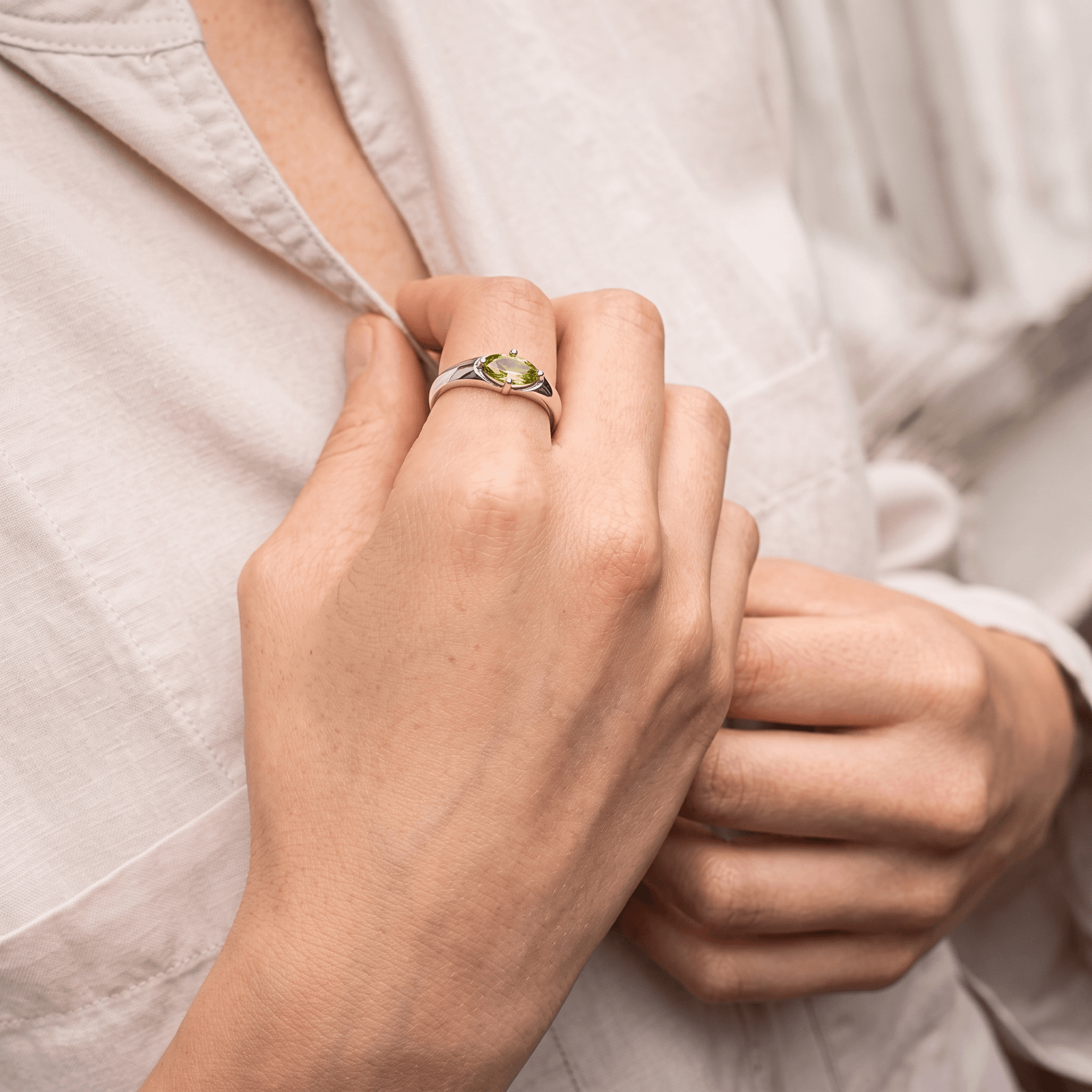 East-west marquise peridot ring worn on a hand holding the collar of a light-colored shirt.