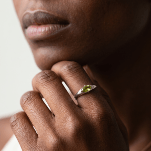 Close-up of a marquise peridot ring on a hand resting beneath the chin, highlighting the green facets and silver-colored band.