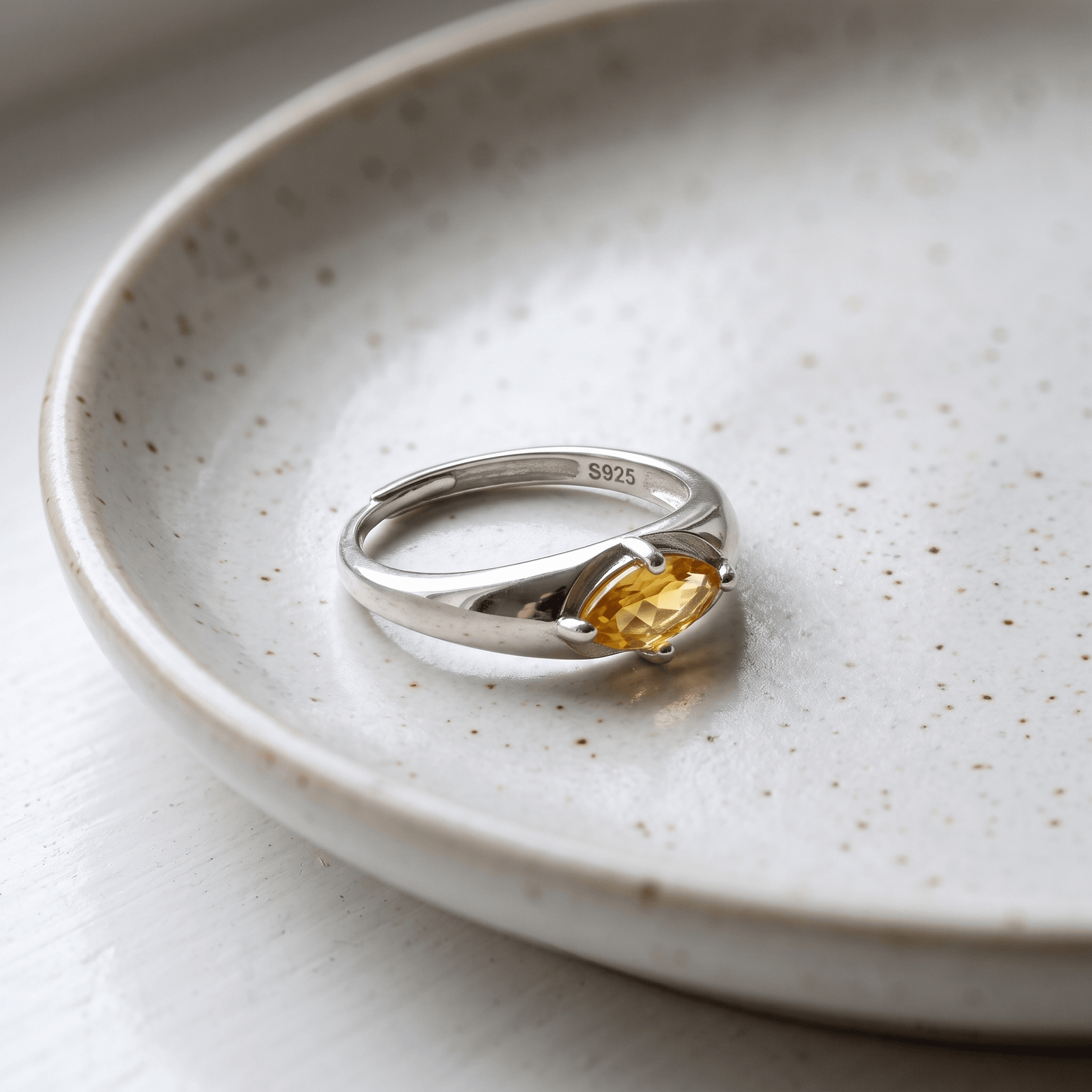 Angled view of a citrine ring on a white speckled dish, showing the overlapping open band and S925 stamp inside.