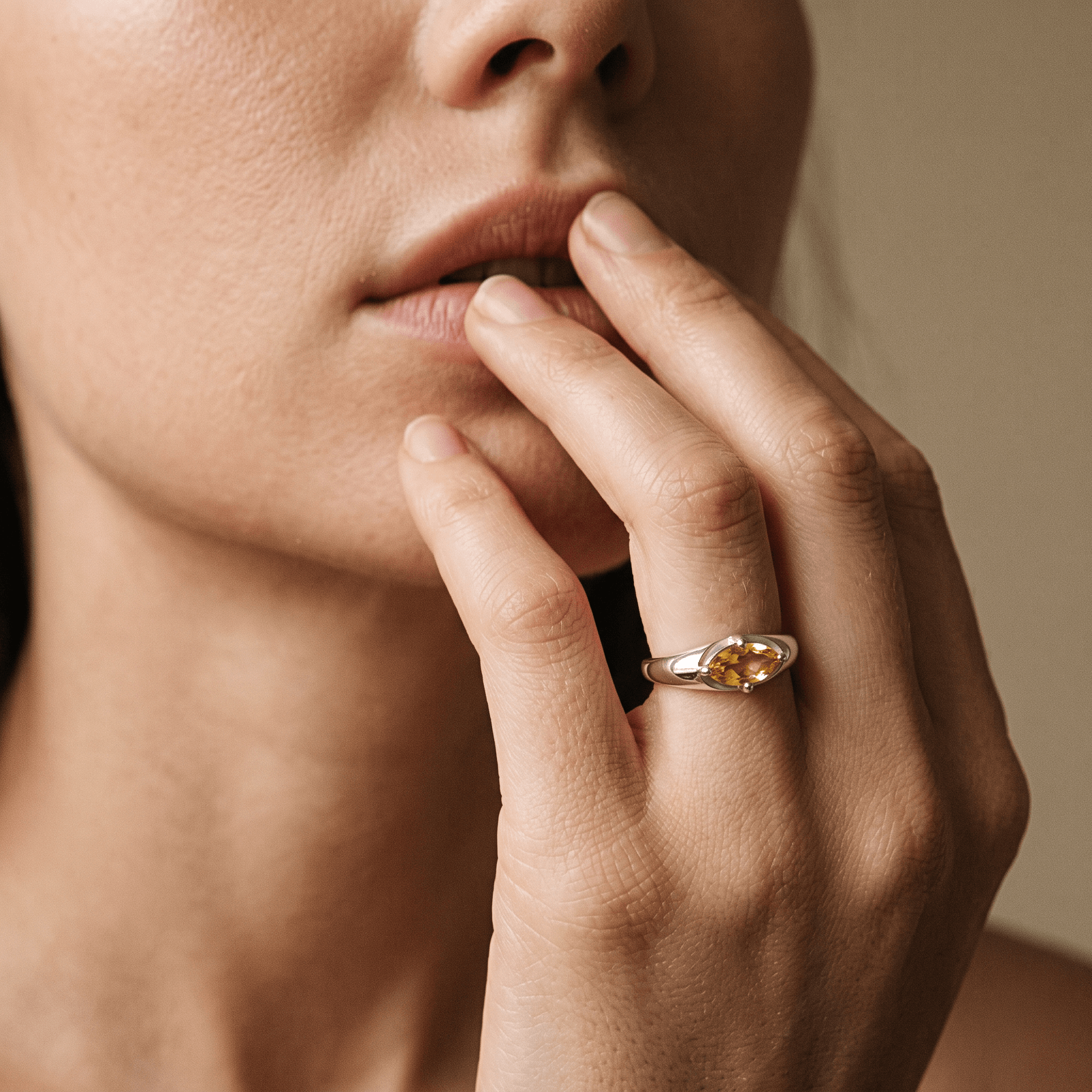 Close-up of a golden-yellow citrine ring worn on a hand raised to the lips in warm light.