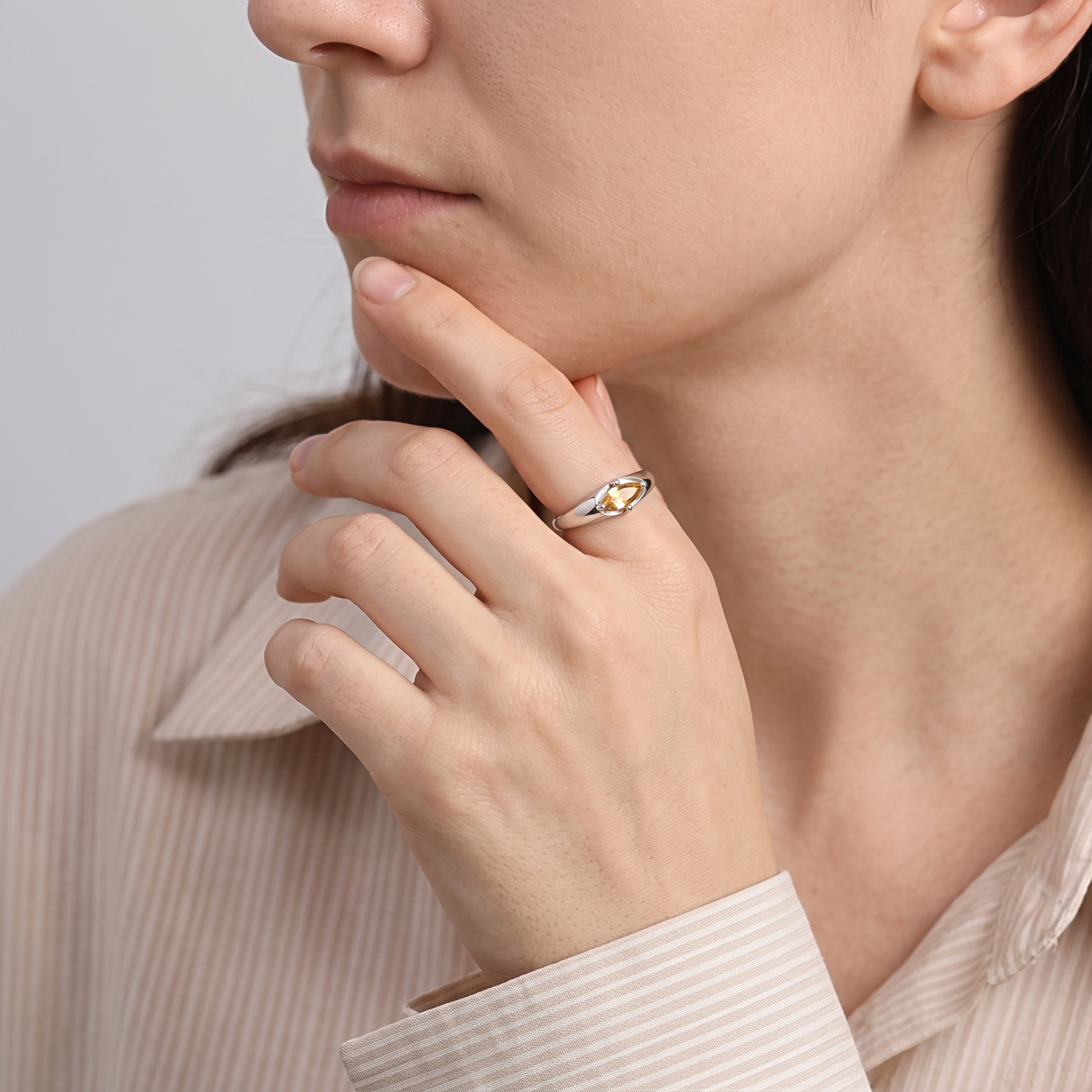 East-west citrine ring worn on a finger resting against the chin, styled with a light striped shirt.